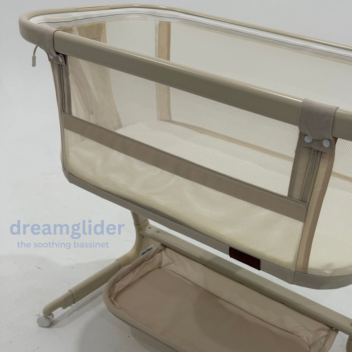 Dream Glider Beige Bassinet positioned beside a bed showing adjustable height and extendable legs